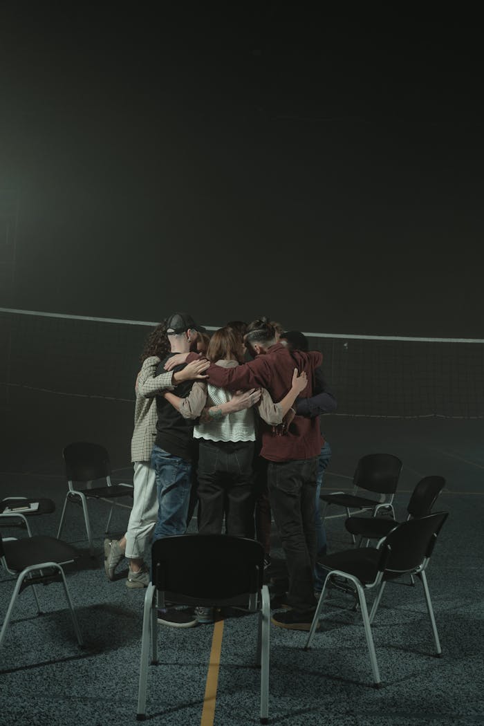 Home A small group of diverse adults embracing in a supportive circle indoors, symbolizing unity and support.