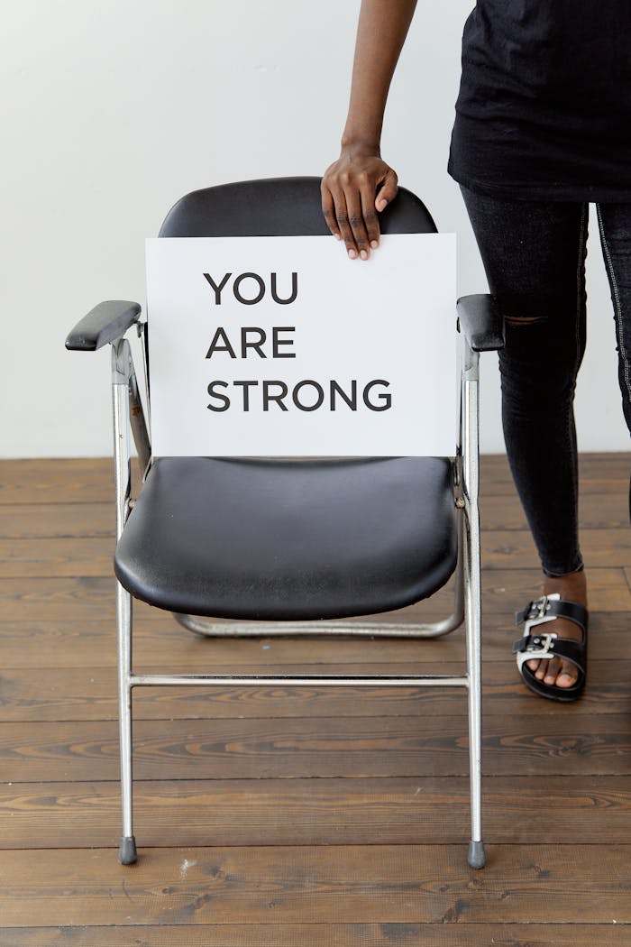 Home A person holds a card with You Are Strong on a chair, symbolizing support and empowerment.